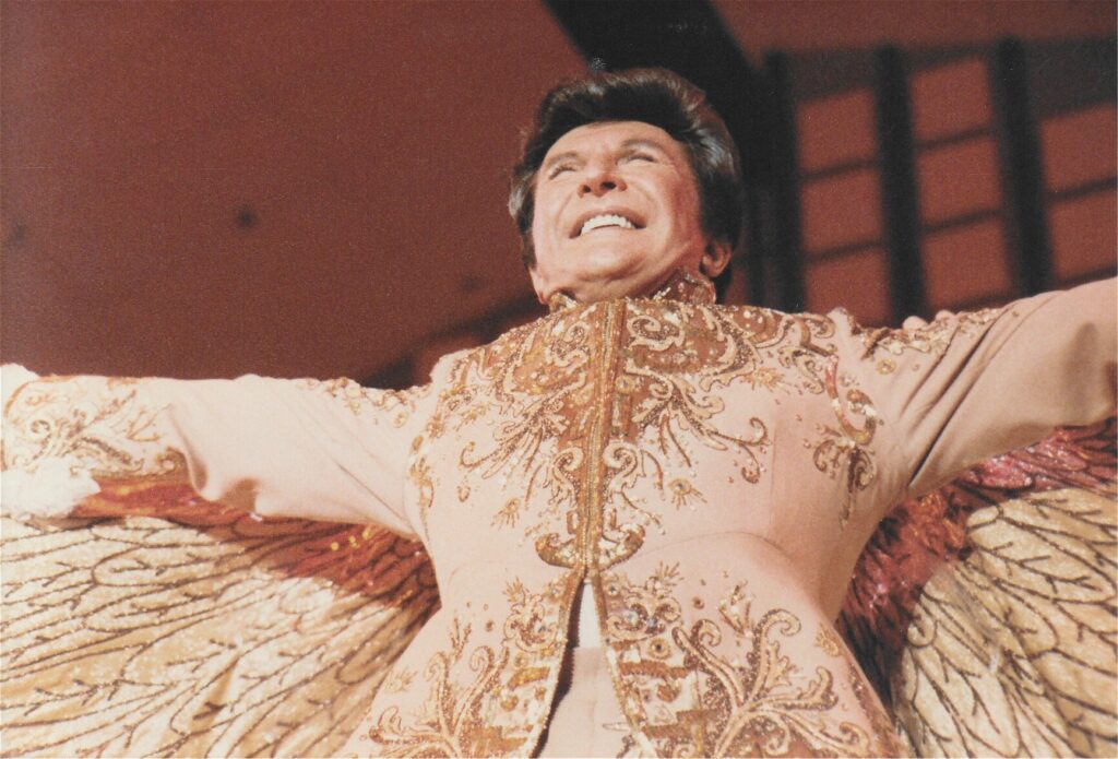 Liberace, wearing a heavily embroidered suit with matching cape, on October 12, 1983 at Palmer Auditorium in Davenport, Iowa